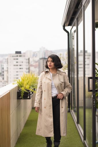 A vertical shot of the young woman in a cream coat standing on the terrace.
