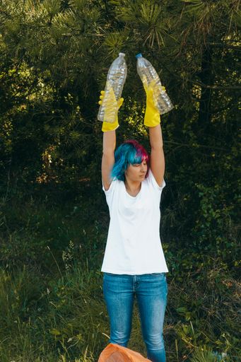 A female with blue and pink hair wearing gloves holding recyclable plastic bottles - plastic pollution concept