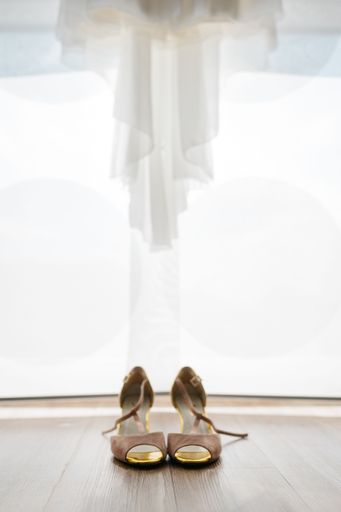 Elegant bridal shoes placed under a flowing wedding dress, set against a soft, diffused light background.