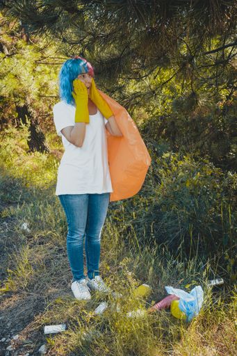 A volunteer female with a shocked face cleaning the environment from plastic pollution holding a garbage bag