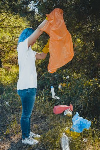 A female emptying the plastic garbage bag in a green environment - plastic pollution concept