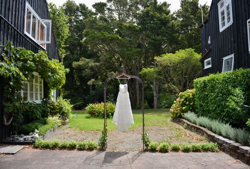 An elegant white bridal dress hanging from a hanger in the garden