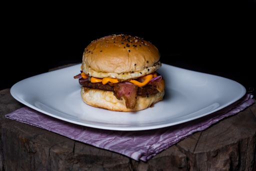 A closeup of a delicious burger on a white plate on a tree trunk on a black background