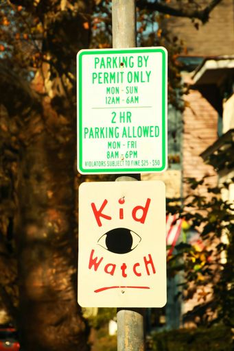 Parking sign next to a 'kid watch' sign on a pole