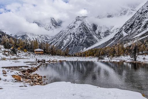 A shot of a cold water lake underneath the snowy mountains and cloudy sky