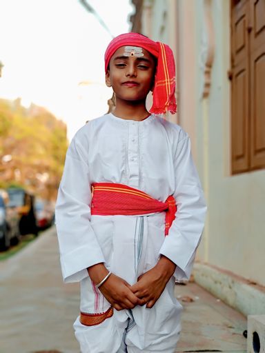A vertical shot of a smiling South Asian boy standing in the street