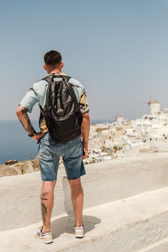 A closeup shot from the back of a Caucasian (White) tourist standing by the sea in Santorini, Romania