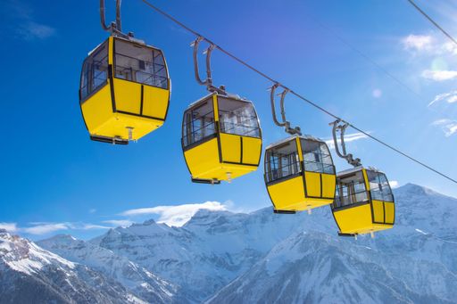 A yellow cable cars against a backdrop of snow-covered mountains and clear blue sky in a winter landscape.