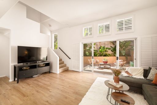 A living room setting with a fireplace and a TV set under the staircase in neutral tones