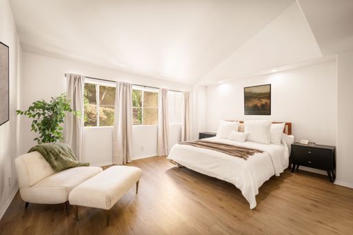 A minimalist bedroom with neutral tones, large windows, modern decor, soft lighting, and cozy furnishings