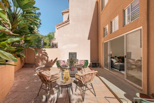 A tropical outdoor patio with lush greenery, terracotta tiles, wicker furniture, and a cozy seating area for relaxation