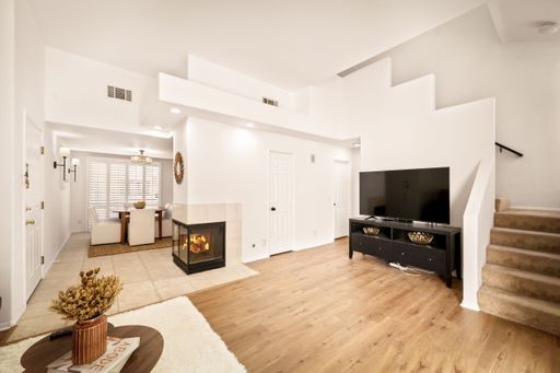 A living room setting with a fireplace and a TV set under the staircase in neutral tones