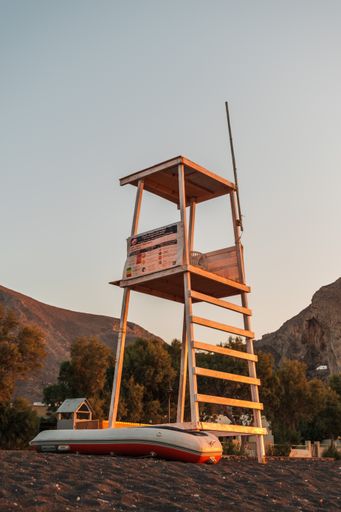 A vertical shot of a wooden lifeguard station and an inflatable boat on a beach in Santorini, Greece
