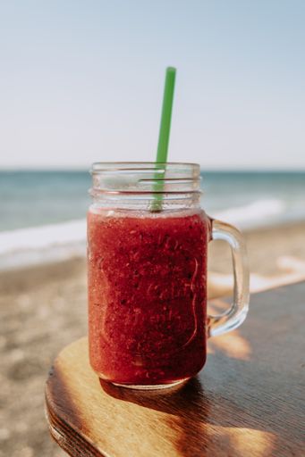 A vertical shot of a glass of smoothie on a table on the beach in Santorini, Greece