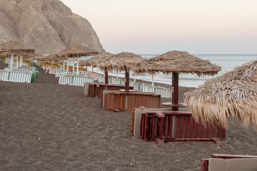 The closed sun loungers and umbrellas on a beach in Santorini, Greece during sunset