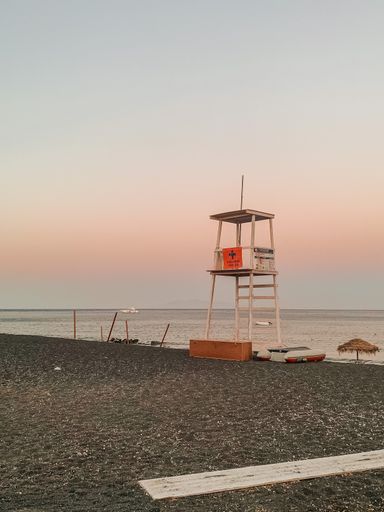 A vertical shot of a lifeguard tower on an empty beach during sunset in Santorini, Greece