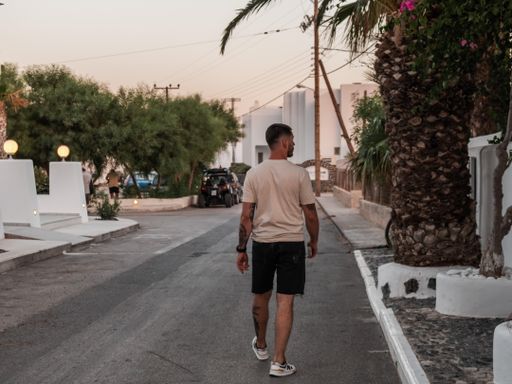 A closeup shot from the back of a Caucasian (White) tourist walking in street in Santorini, Romania