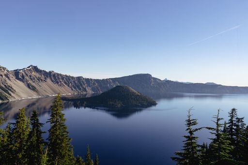 A scenic view of Crater Lake National Park with calm blue waters, rugged cliffs, and lush green trees