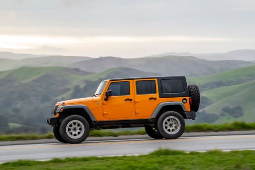An orange SUV driving on a scenic road with rolling green hills in the background.