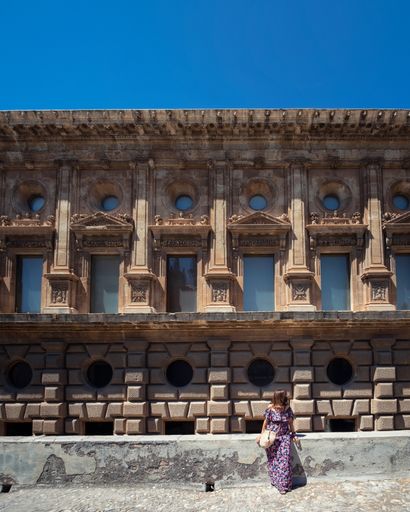 A Caucasian woman with a long summer dress posing in front of the Palace of Charles V
