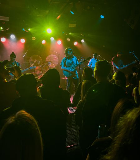 A band performs on stage under vibrant green and yellow lights with a crowd watching