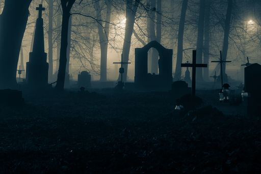 Eerie graveyard scene with tombstones and crosses silhouetted against a misty forest backdrop, creating a mysterious atmosphere.