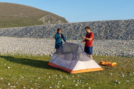 Two young Caucasian tourists in sportswear setting up a tent at a campsite surrounded by rocks in nature