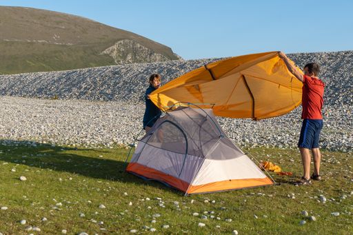 Two young Caucasian tourists in sportswear setting up a tent at a campsite surrounded by rocks in nature