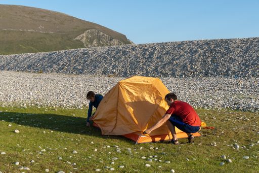 Two young Caucasian tourists in sportswear setting up a tent at a campsite surrounded by rocks in nature