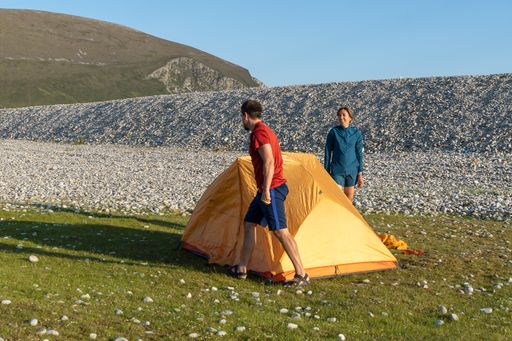 Two young Caucasian tourists in sportswear setting up a tent at a campsite surrounded by rocks in nature
