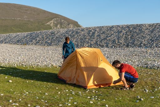 Two young Caucasian tourists in sportswear setting up a tent at a campsite surrounded by rocks in nature