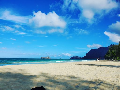 Scenic view of a sandy beach with clear blue waters and mountains under a bright sky, capturing a tranquil coastal landscape.