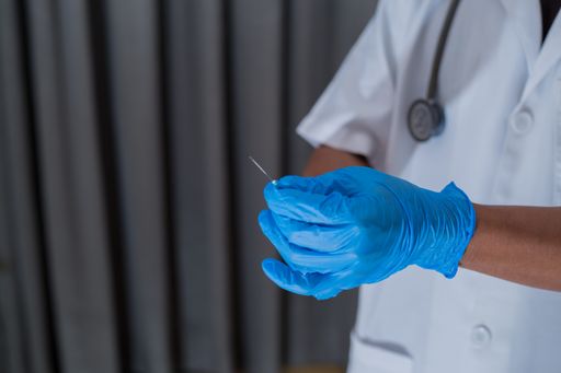 A closeup of a doctor with a stethoscope around his neck holding a syringe with medical gloves