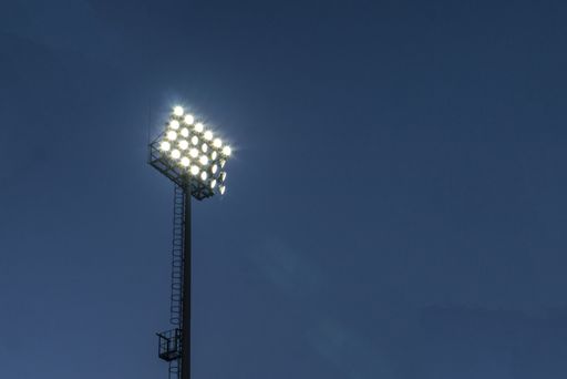 A low angle closeup shot of stadium lights under a dark blue sky