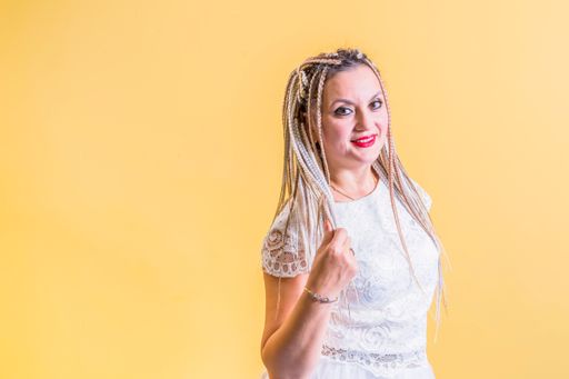 Happy young woman with African braids on her head, in a white dress, stands on a yellow background. Looks into the camera.