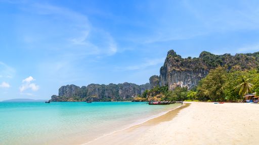 Railay beach west with exotic limestone cliff mountain and longtail wooden tourist boat, Krabi, Thailand