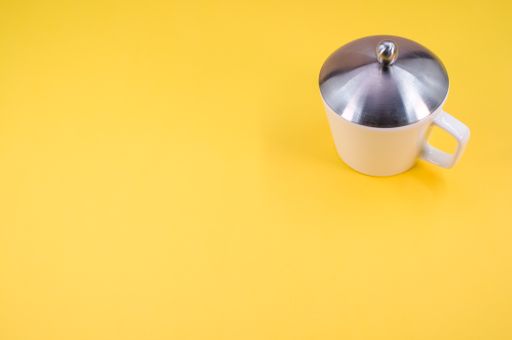A closeup shot of a white mug with a lid on a yellow background