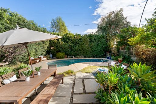 A luxurious backyard with a serene swimming pool, lush greenery, a spacious patio, and stylish outdoor seating for relaxation.