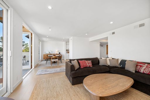 Contemporary living room with an L-shaped sectional, warm-toned decor, and floor-to-ceiling windows leading to an outdoor patio