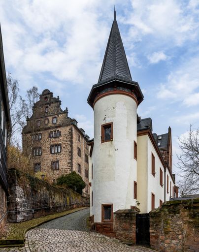 Historic European castle with a tower and cobblestone path under a partly cloudy sky.