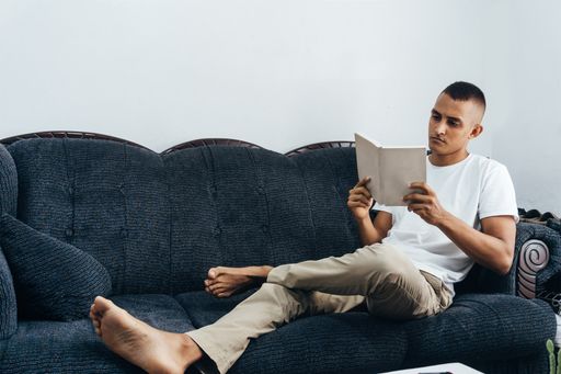 A young Hispanic male sitting on the sofa and reading a book