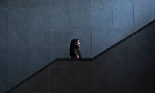 A side view of a young dark-haired woman standing on the staircase on a gray wall background - future and unknown concept