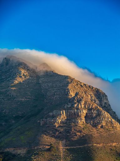 A stunning view of a mountain peak with a cloud draping over it under a vivid blue sky, showcasing nature's beauty.