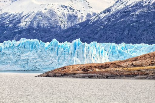 A vertical shot of glacier with rocky land and a mountain in the foreground