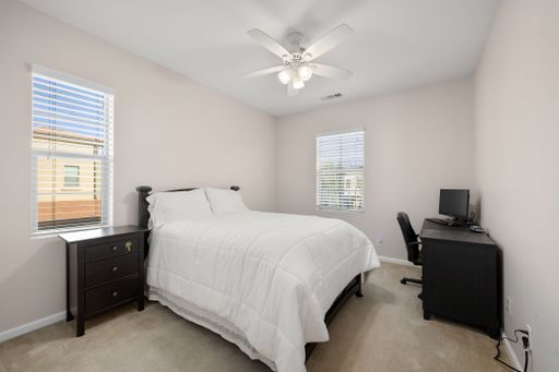Neutral-toned bedroom with a neatly made bed, dark wood furniture, and a small desk setup for work or study