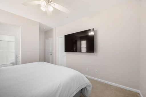 Neutral-toned bedroom with a neatly made bed, dark wood furniture, and a small desk setup for work or study