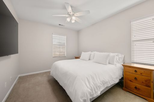 Neutral-toned bedroom with a neatly made bed, dark wood furniture, and a small desk setup for work or study