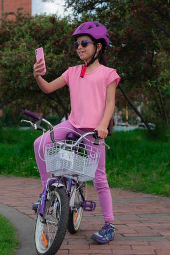 A vertical shot of a girl checking her cell phone when she is on her bike in the park