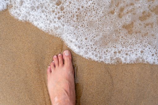 A top view of a male foot on the sand of a seashore