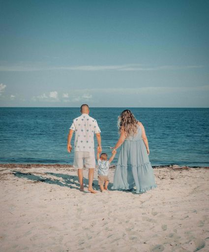 a vertical shot of rear family of mother, father, baby walking to water on sand beach under sunlight